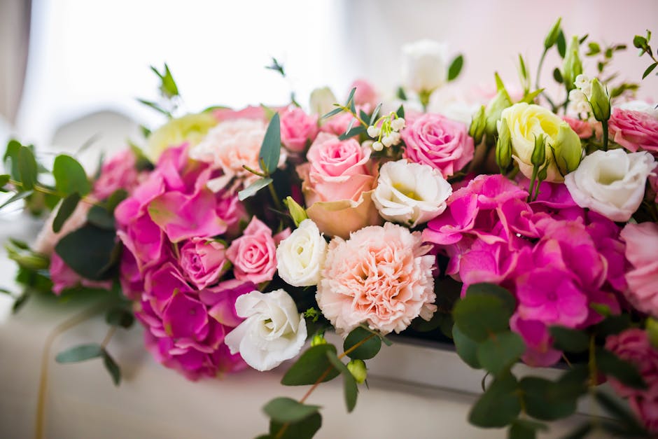 A floral arrangement featuring a lush bouquet of fresh flowers, predominantly pink and white roses, complemented by pale pink carnations, white lisianthus, and sprigs of greenery such as eucalyptus le