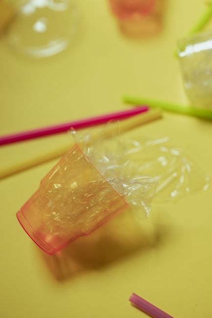 A clear plastic flower wrapper partially peeled away, revealing the bouquet inside that features a mix of fresh, vibrant flowers including pink roses, white lilies, and purple statice, arranged with g